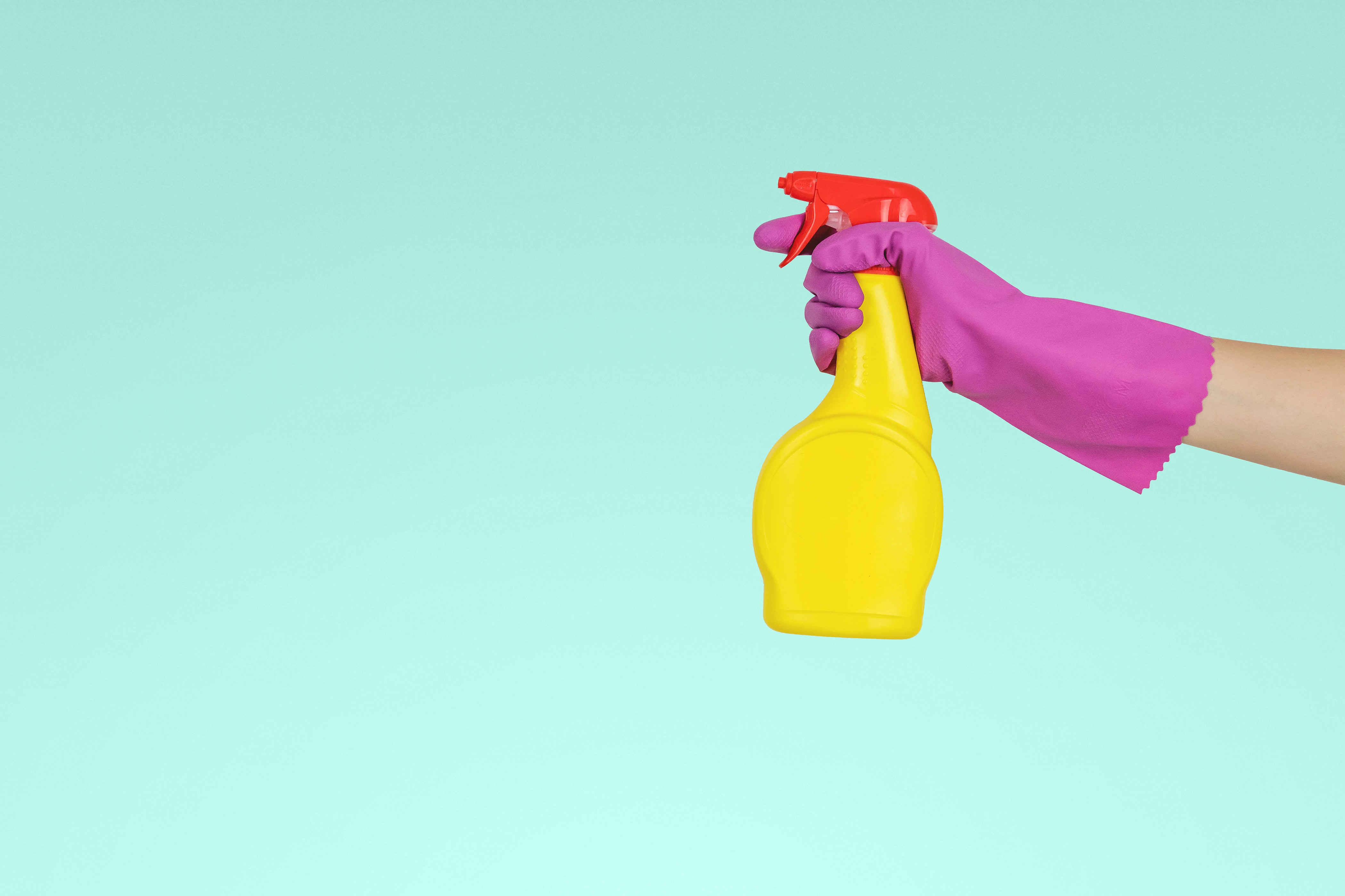 Brightly colored spray bottle held with purple glove over blue background